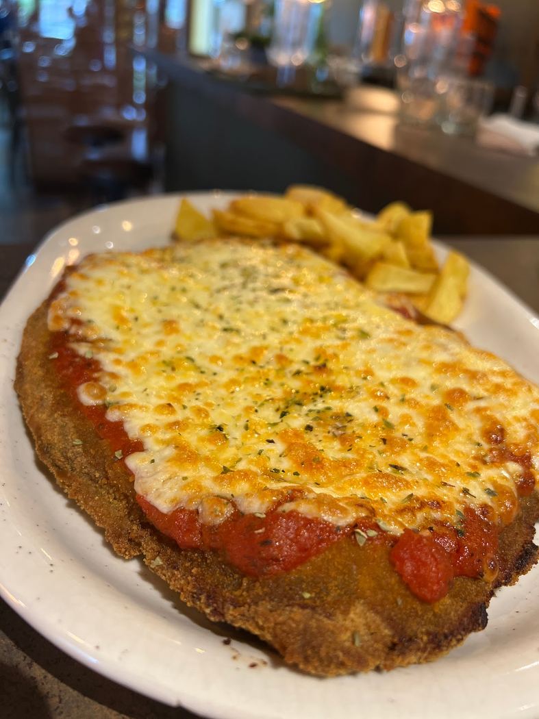 Milanesa a la napolitana con patatas fritas, un plato clásico de carne empanada con tomate y queso gratinado.