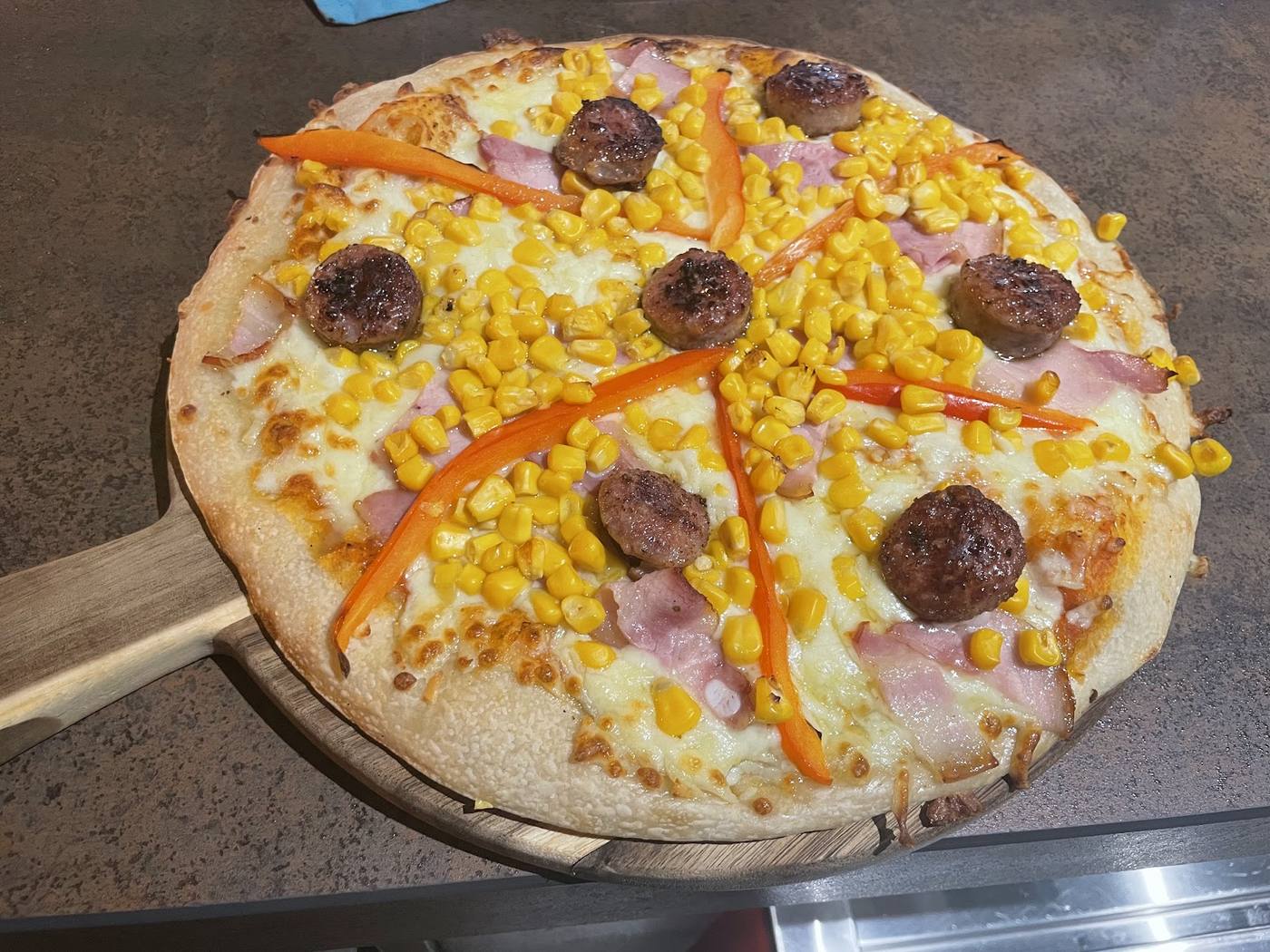 Pizza con maíz, salchicha italiana y pimiento rojo sobre masa fina y crujiente.